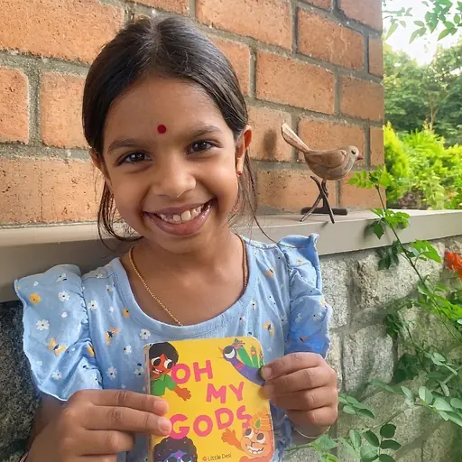 Rukmini holding her copy of the Little Desi board book Oh My Gods